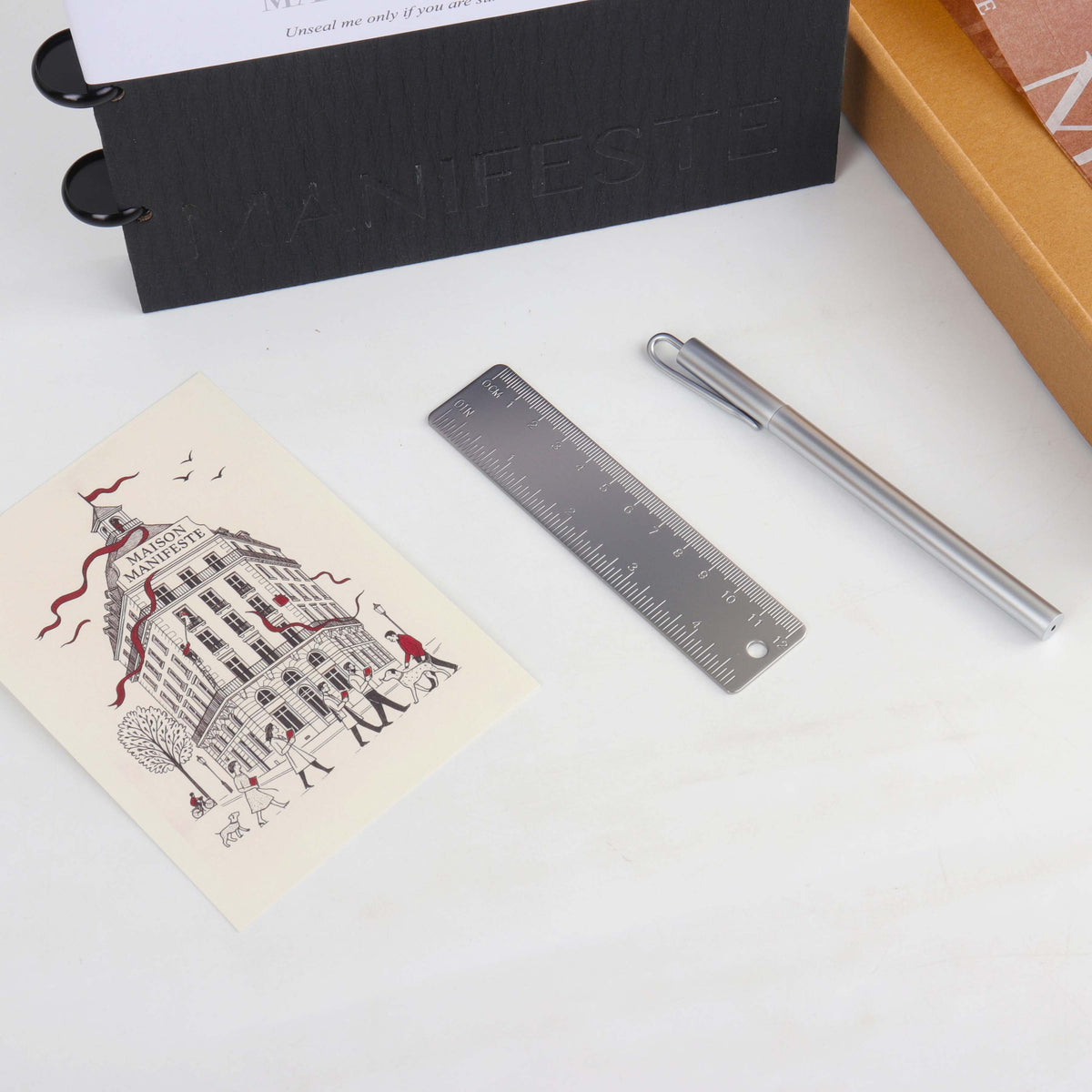 Brass pen and brass ruler laid beside a Maison Manifeste welcome card