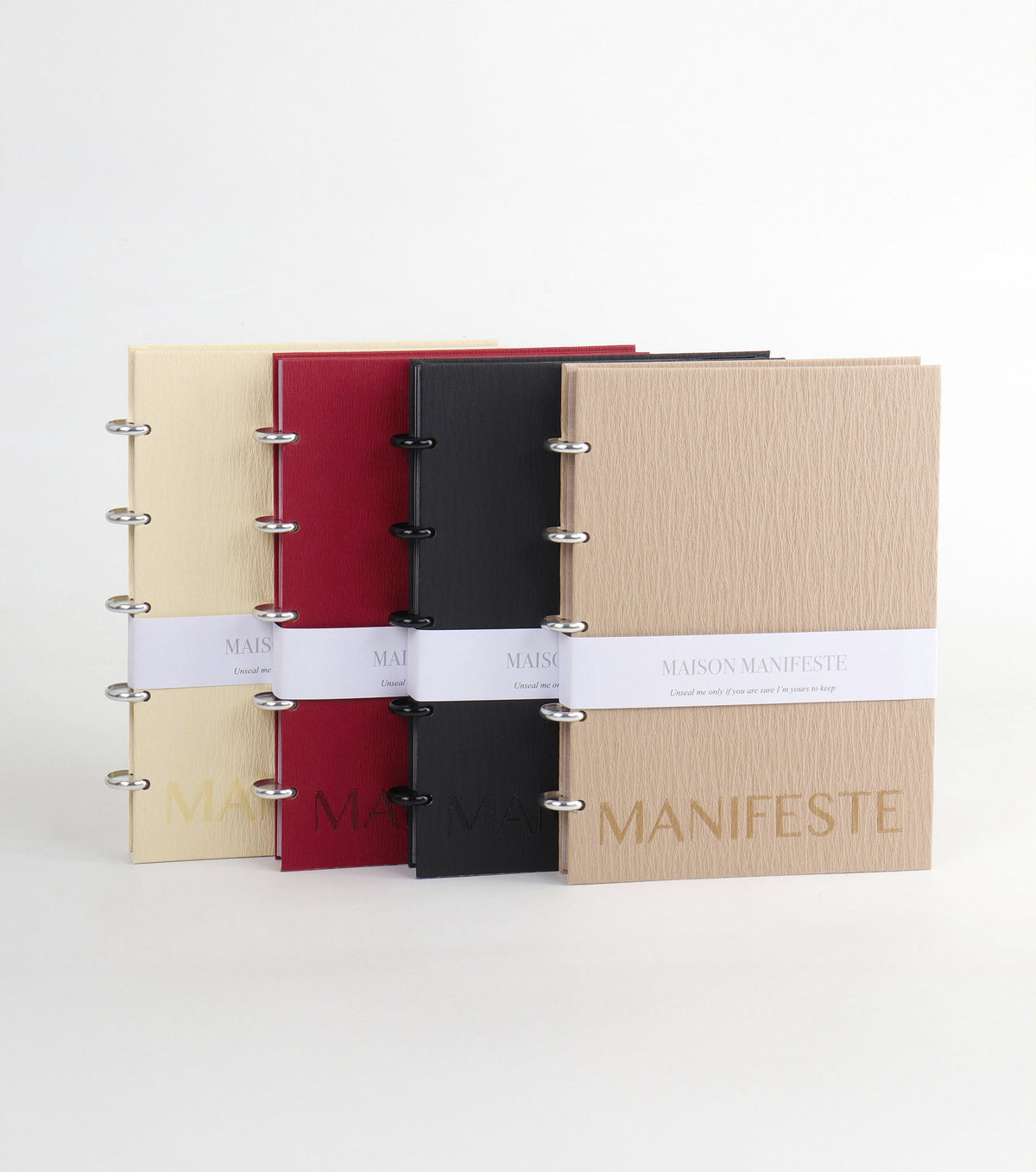 Four binders in beige, red, black, and brown with 'MANIFESTE' branding on a white background.