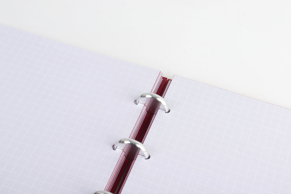 Close-up of the Burgundy notebook’s metal discbound system and grid pages, flat-lay view