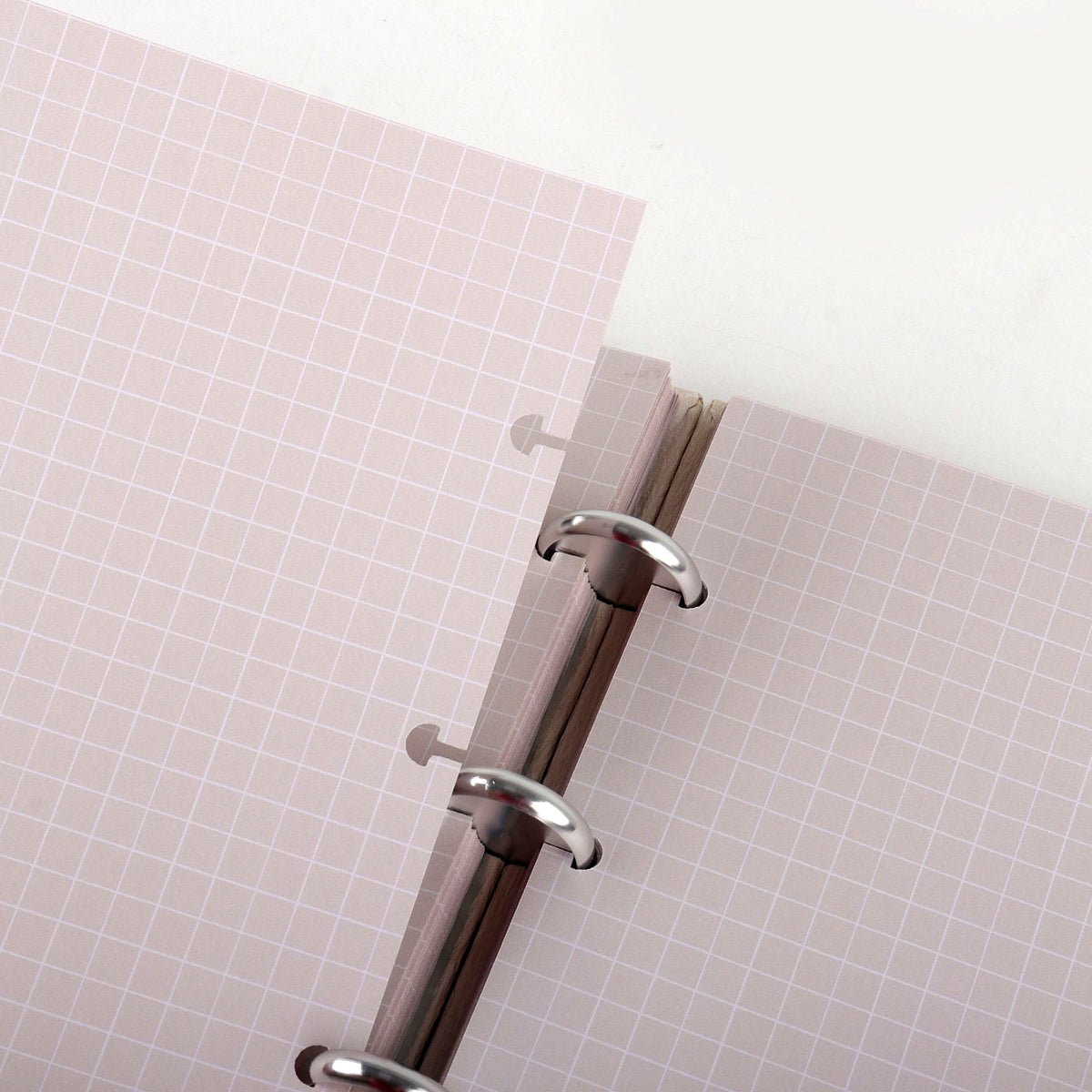 Close-up of a discbound notebook page being detached, showing pink grid paper and modular refill system